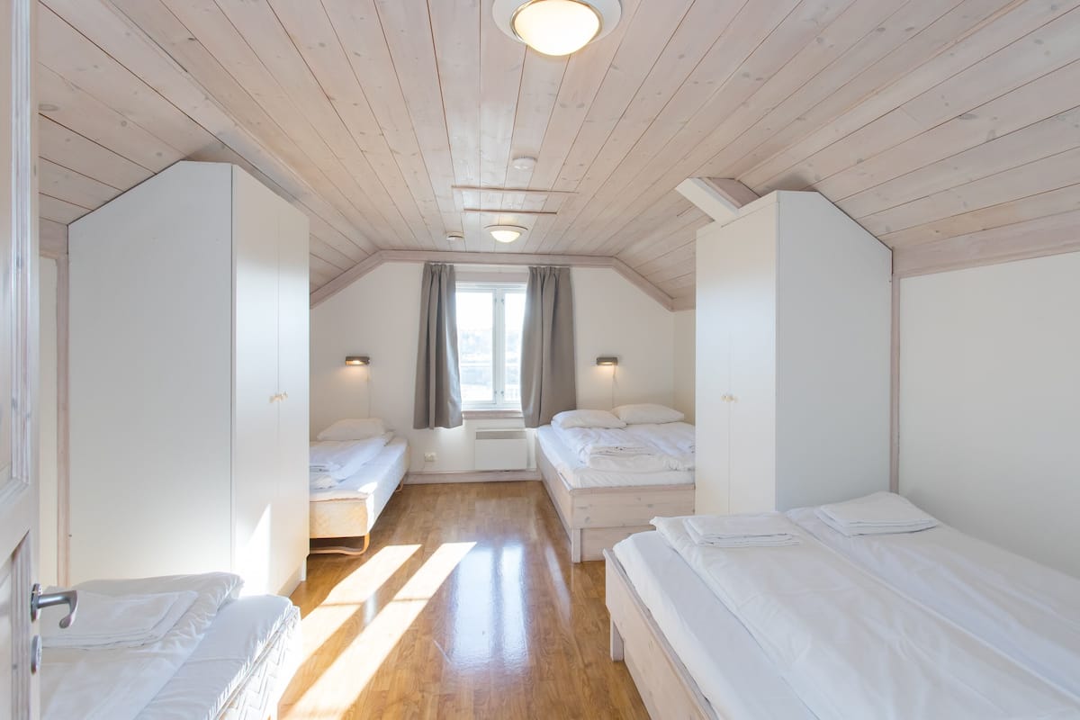 A bedroom with two beds, wooden floors, and a sloped ceiling with recessed lighting.