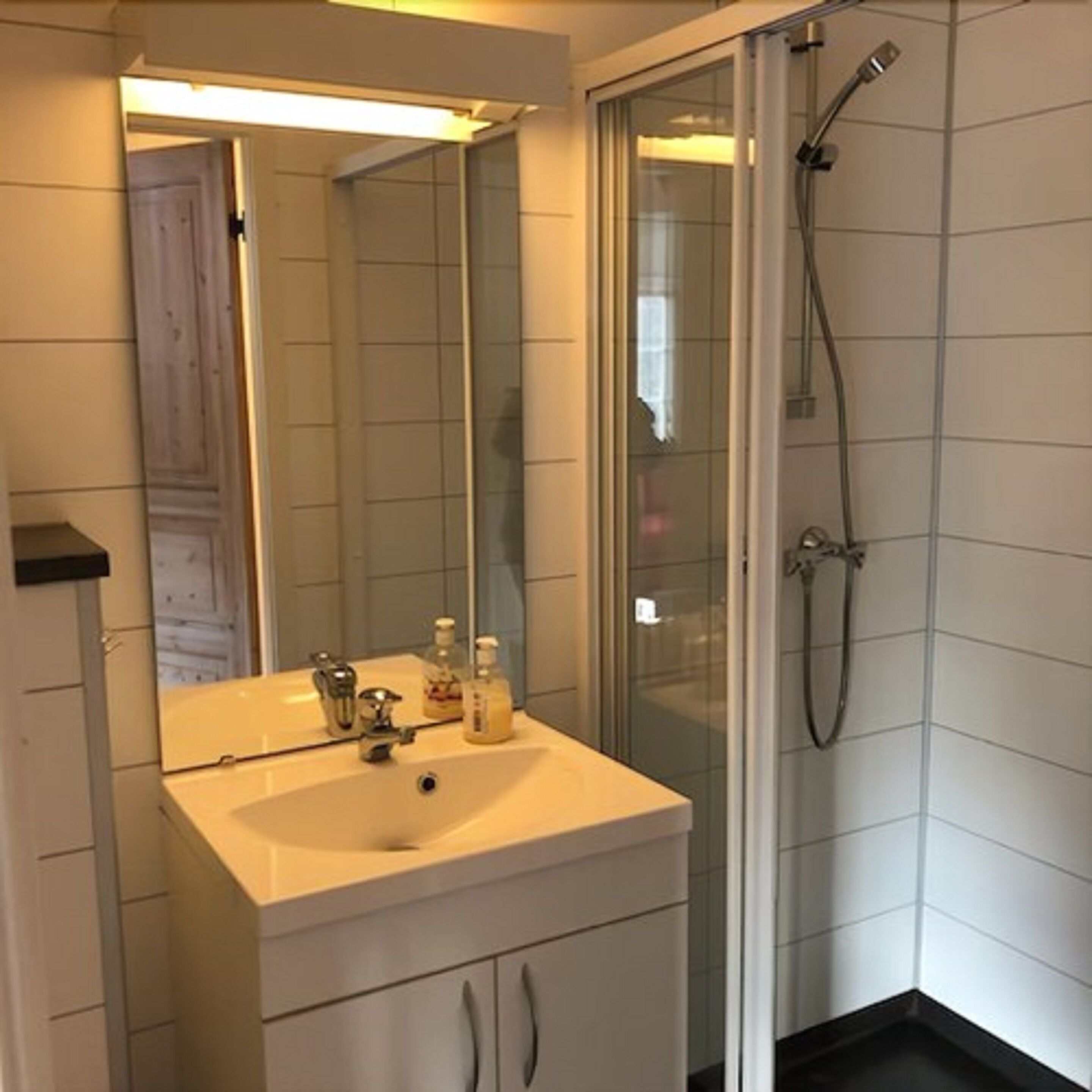 Un baño con lavamanos blanco, espejo y ducha.