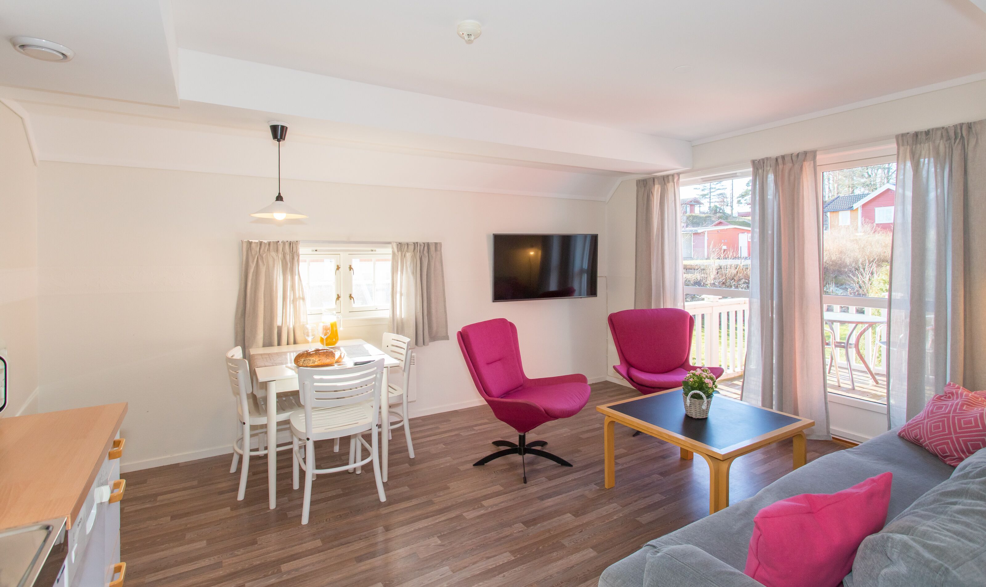 A modern living room with a dining area, a grey sofa, a pink armchair, and a wooden coffee table.