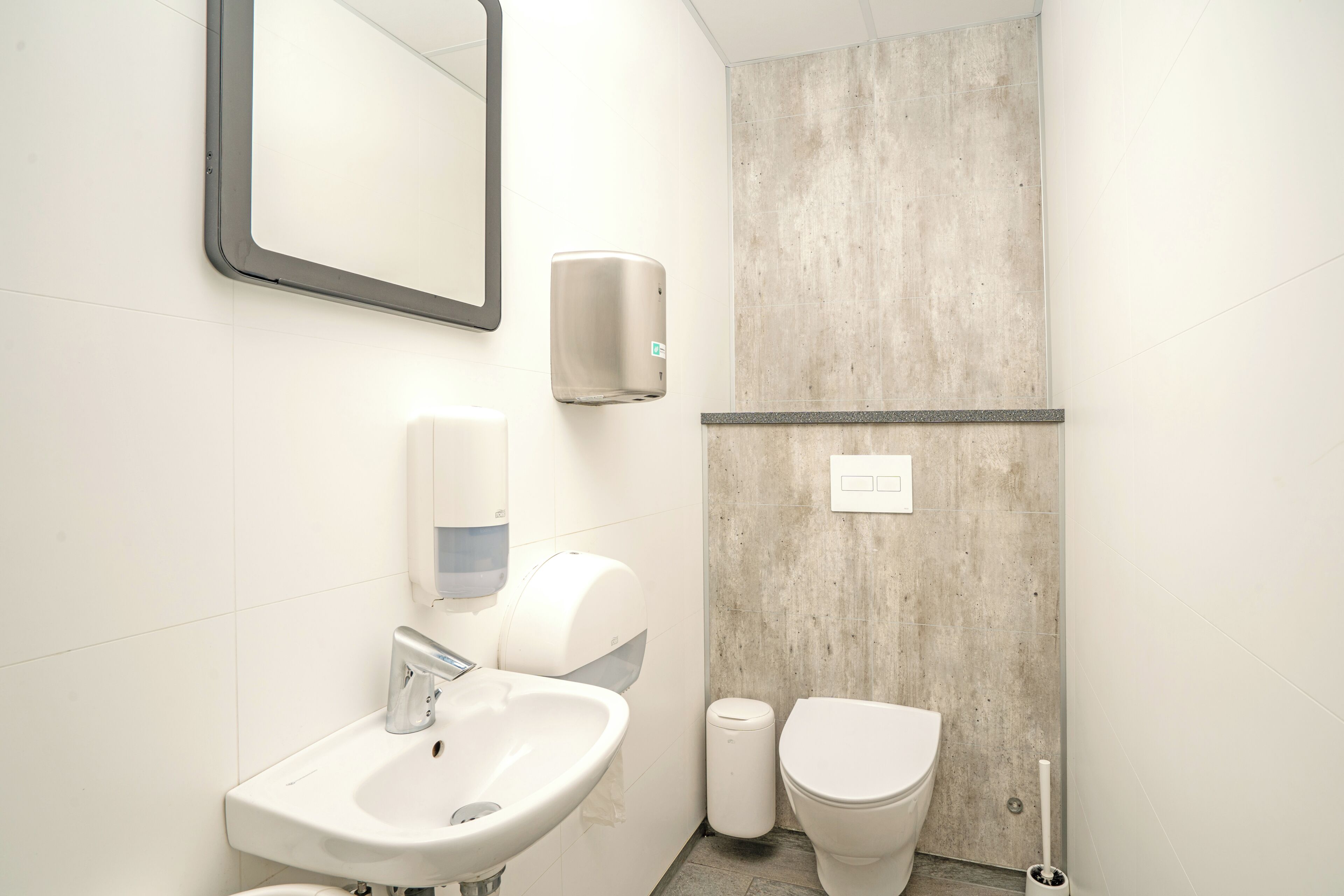 A bathroom with a sink, mirror, hand dryer, and toilet.