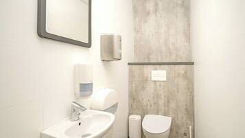 A bathroom with a sink, mirror, hand dryer, and toilet.