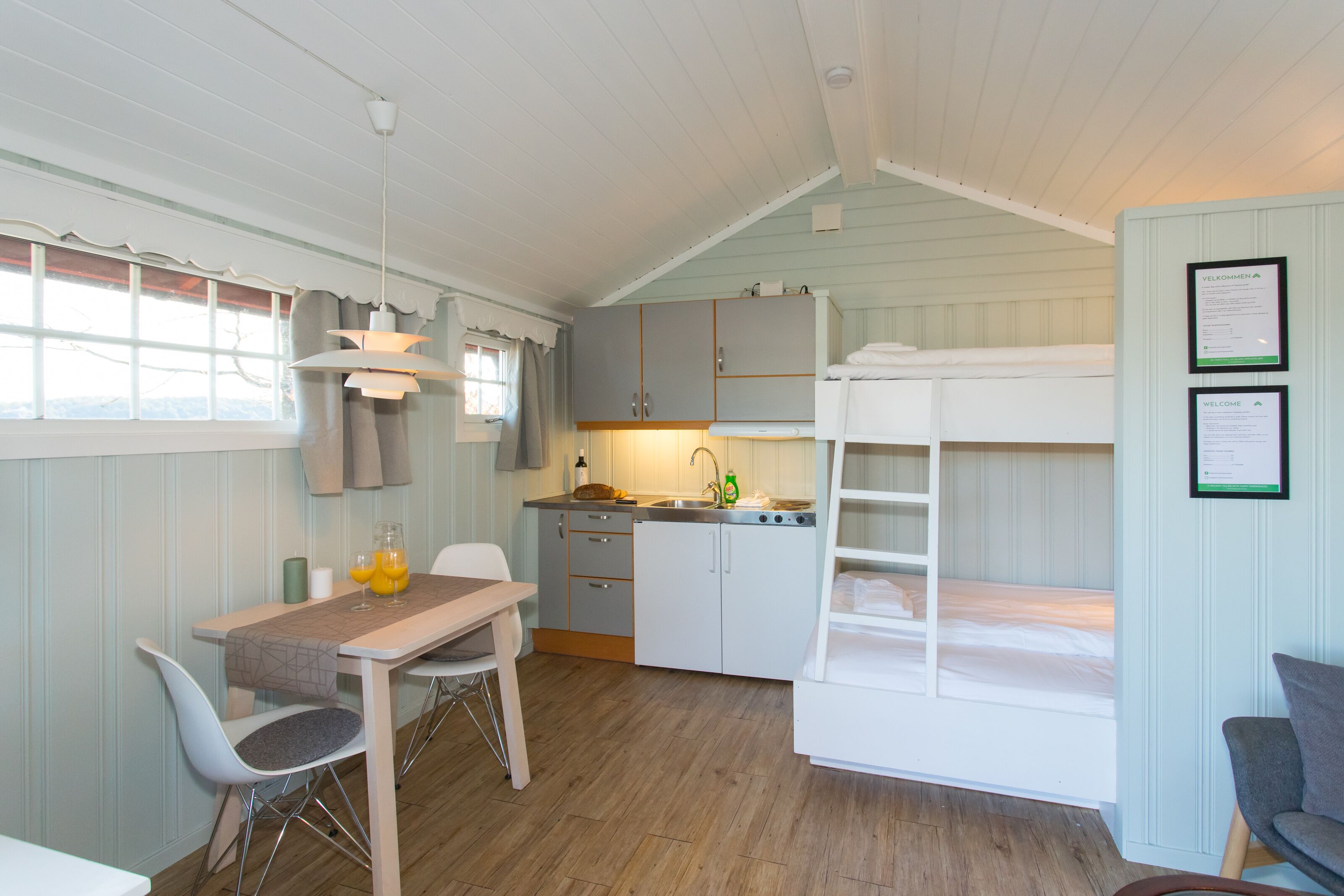 Een kleine kamer met een stapelbed, een kitchenette, een eethoek met tafel en stoelen, en een raam met gordijnen.
