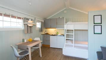 Een kleine kamer met een stapelbed, een kitchenette, een eethoek met tafel en stoelen, en een raam met gordijnen.