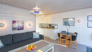 Una sala moderna con un sofá, una mesa de centro de vidrio con fruta, un comedor con mesa y sillas, una cocina con electrodomésticos y obras de arte en las paredes.
