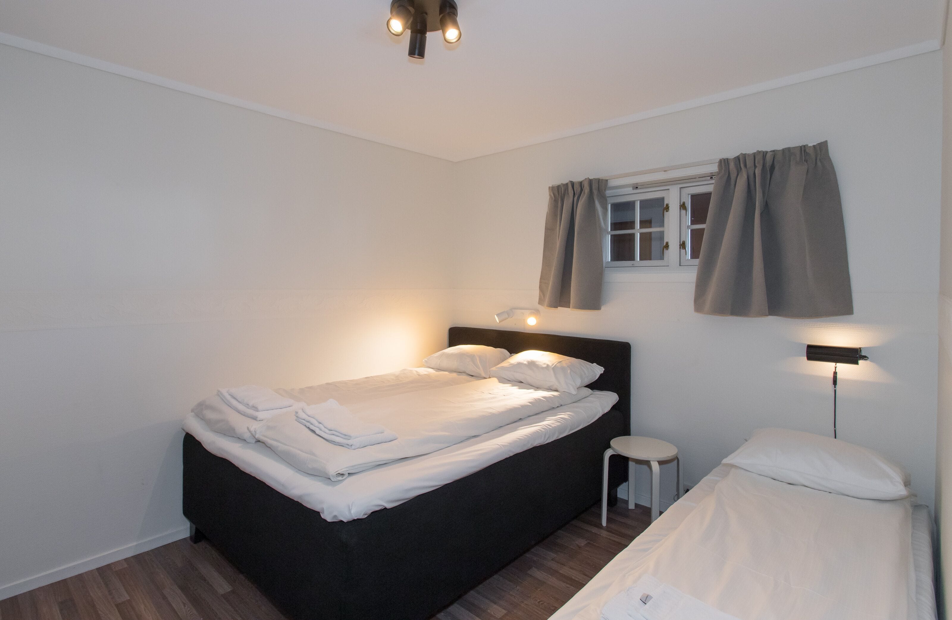 A neatly made bed with white linens, a small bedside table, and a wall-mounted lamp.