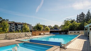 Una piscina rectangular con muelle de madera, sillas de descanso y valla blanca.