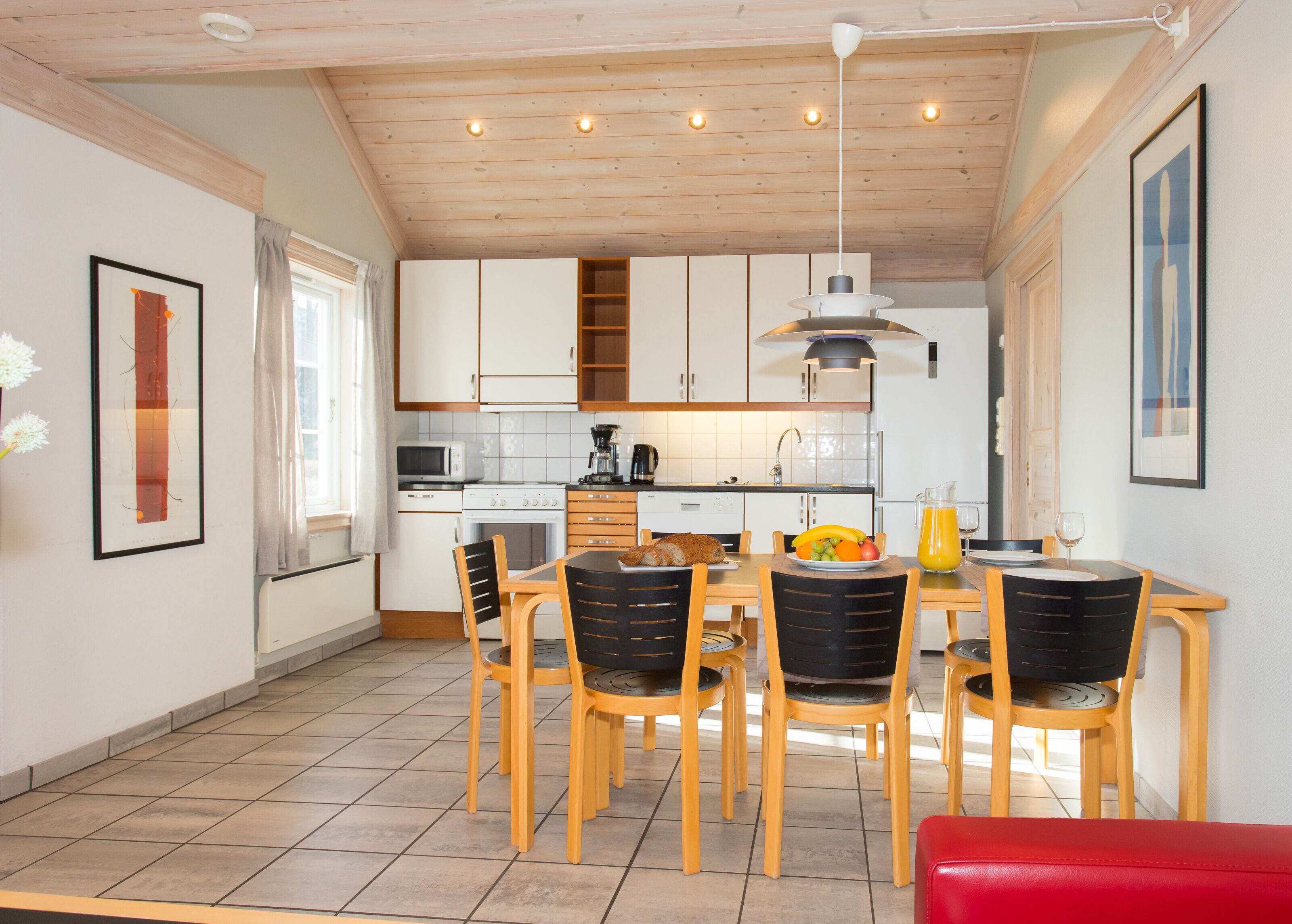 A modern kitchen with white cabinets, a dining table with chairs, and a red bench.