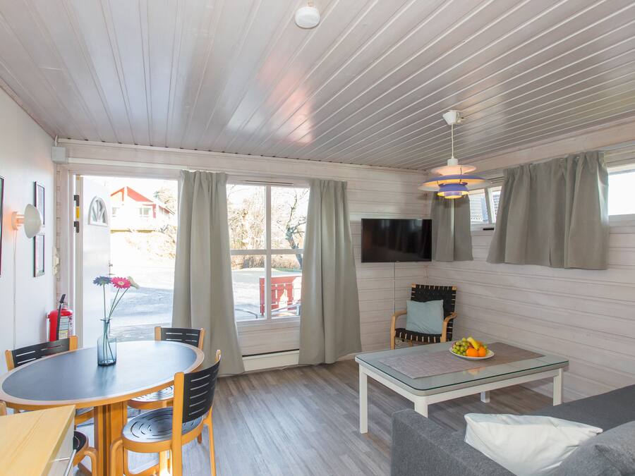 A cozy room with a dining table, chairs, a sofa, a TV, and a window with curtains.