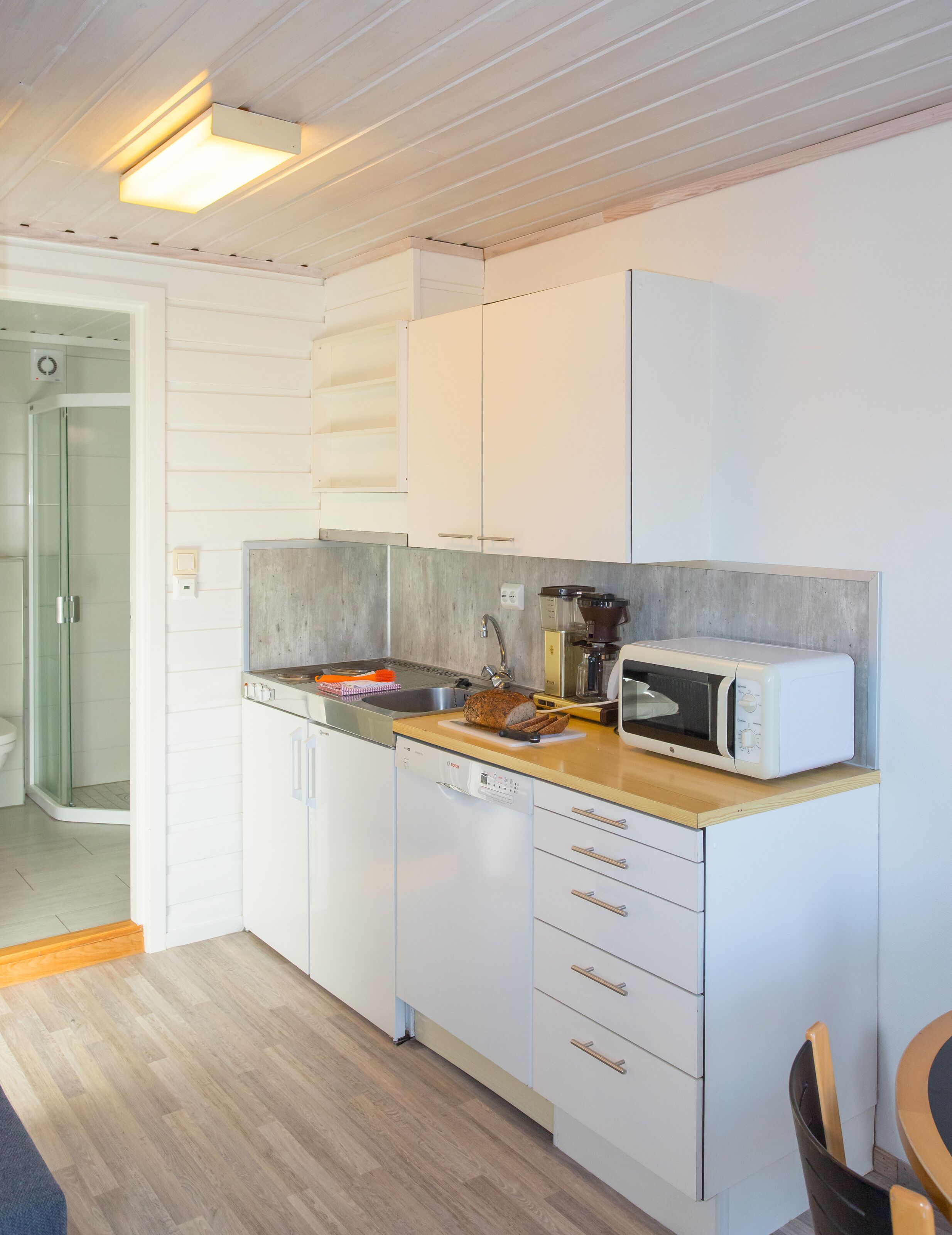 Una cocina compacta con armarios blancos, microondas, lavamanos y encimera de madera.