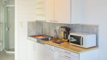 Una cocina compacta con armarios blancos, microondas, lavamanos y encimera de madera.