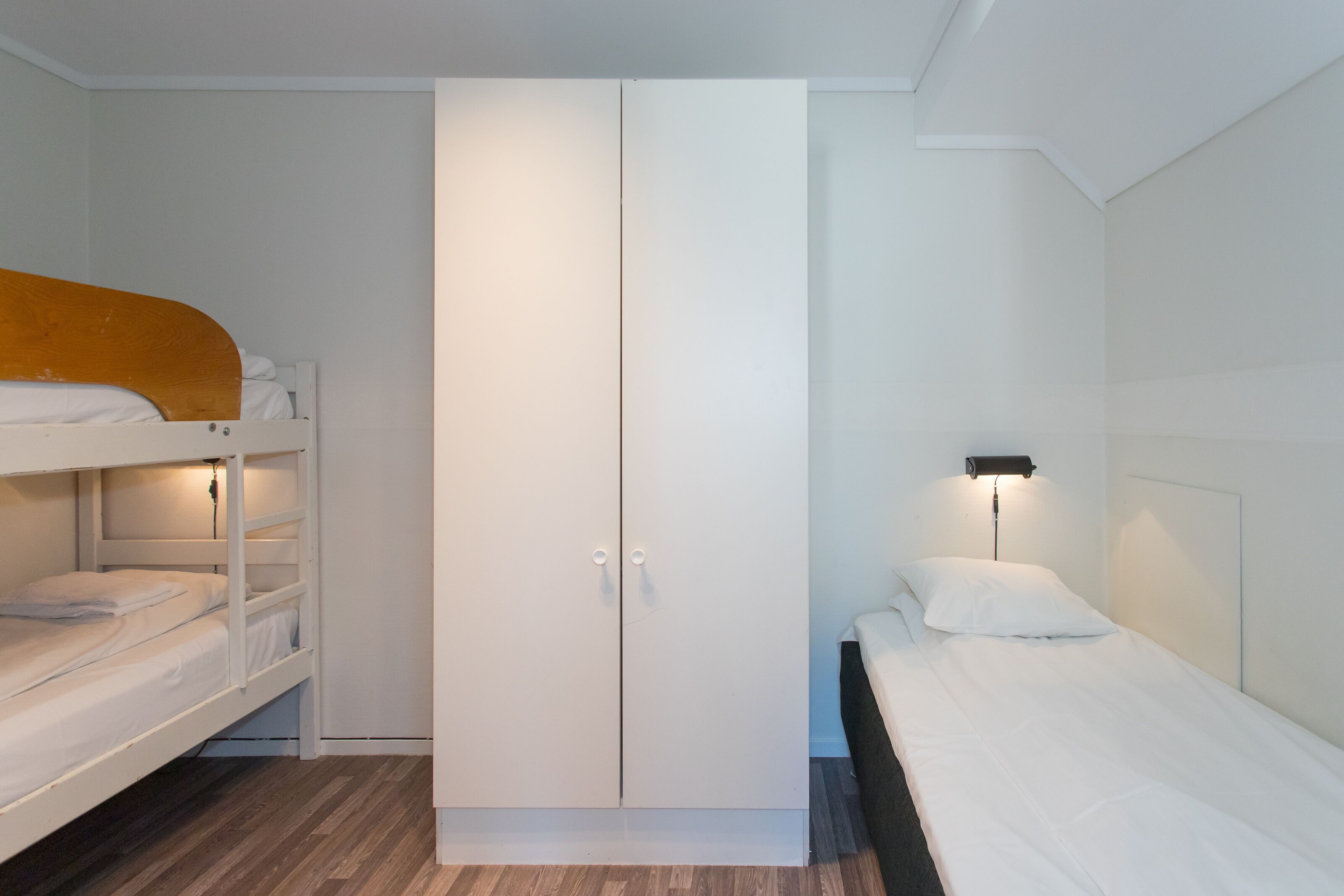 A room with bunk beds, a wardrobe, and a bedside table with a lamp.