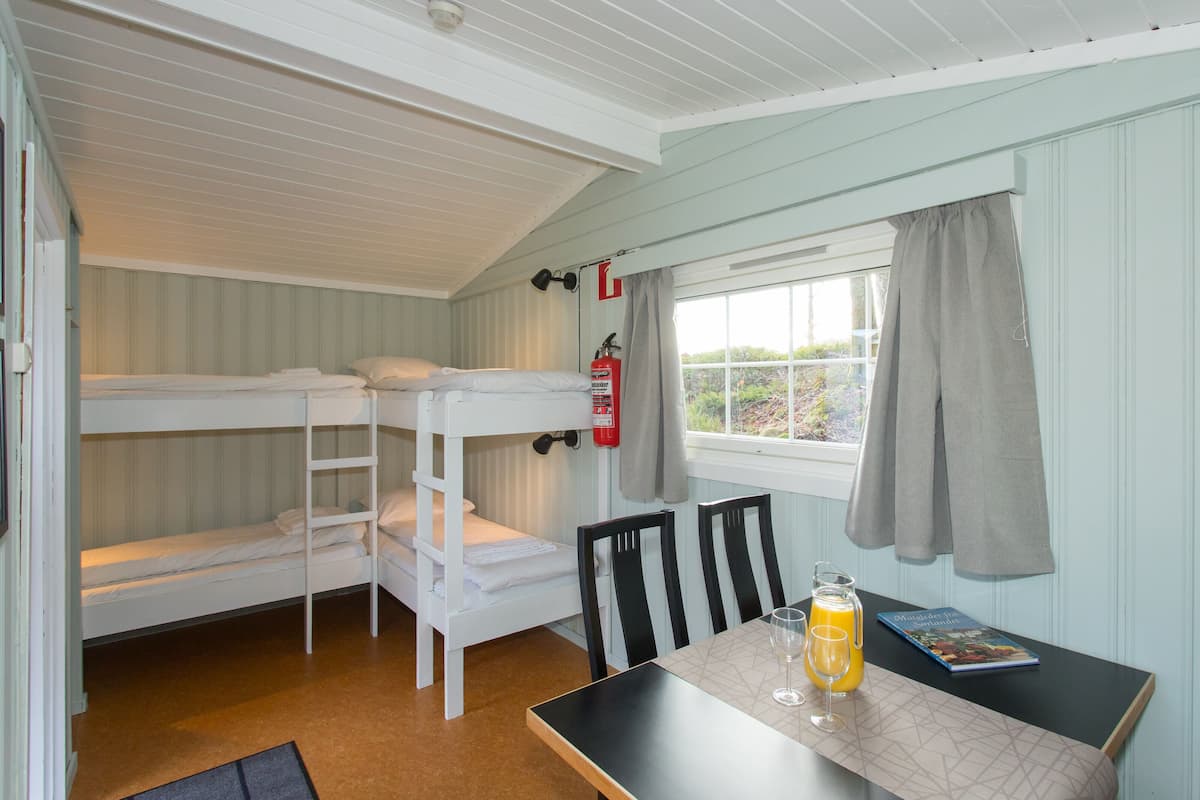 A bunk bed room with a table, chairs, a fire extinguisher, and a window with curtains.