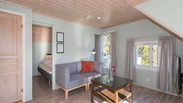 A cozy room with a wooden ceiling, a bed, a grey sofa, a small table, and a window with curtains.