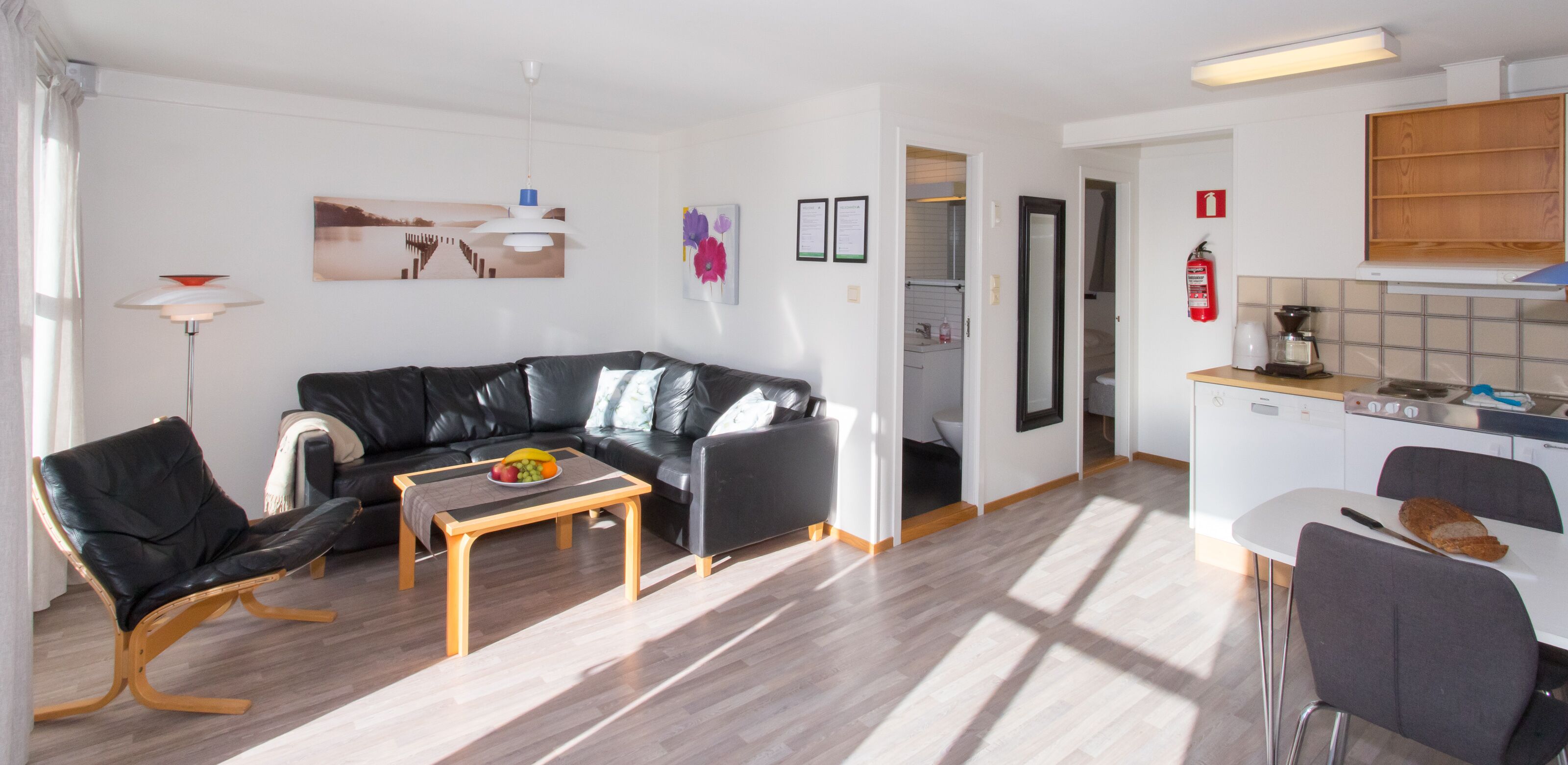 A modern living room with a black leather sofa, a wooden coffee table, and a dining area with a white table and chairs.