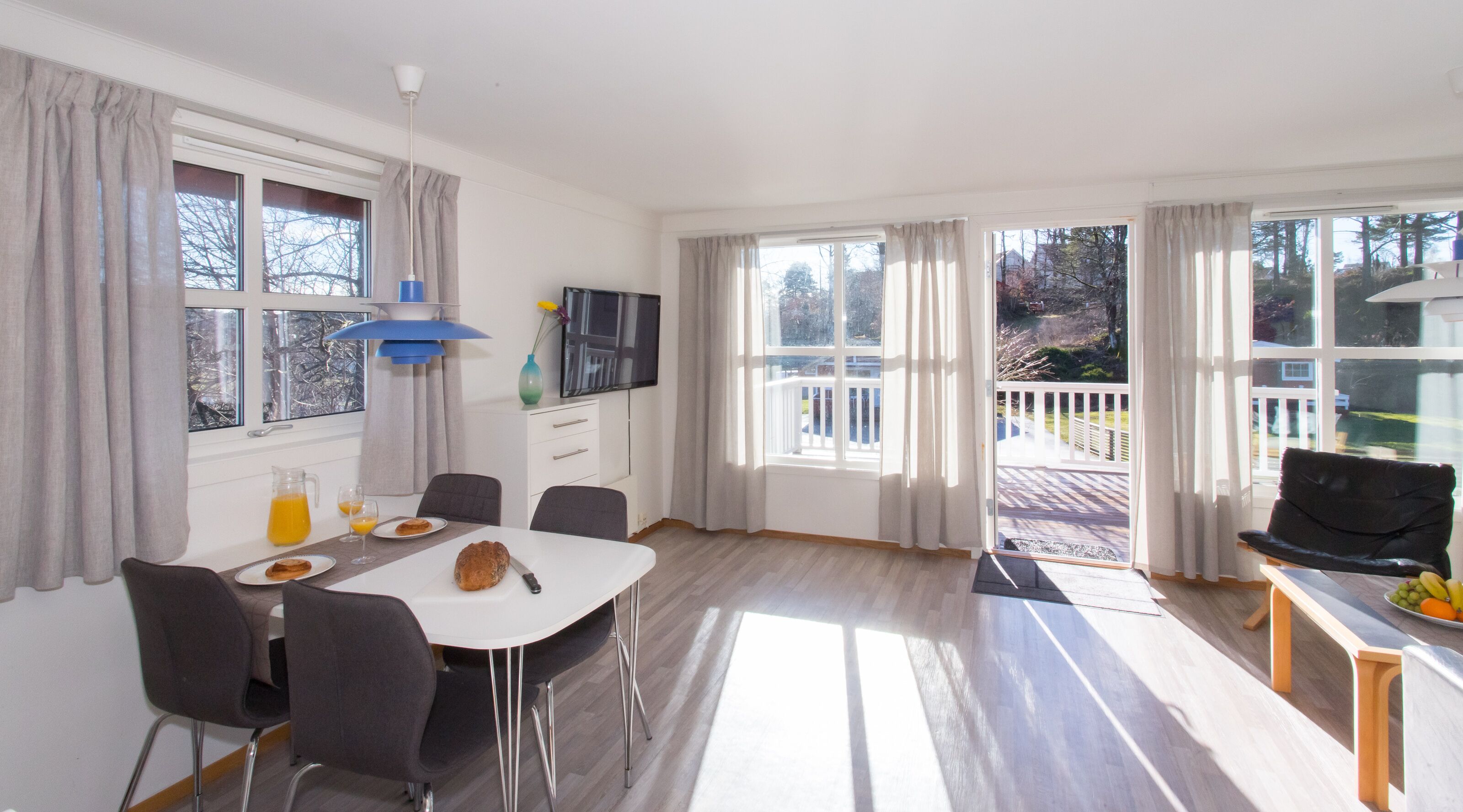 Una habitación luminosa y soleada con una mesa lista para el desayuno, ventanas amplias y un balcón con vistas al exterior.