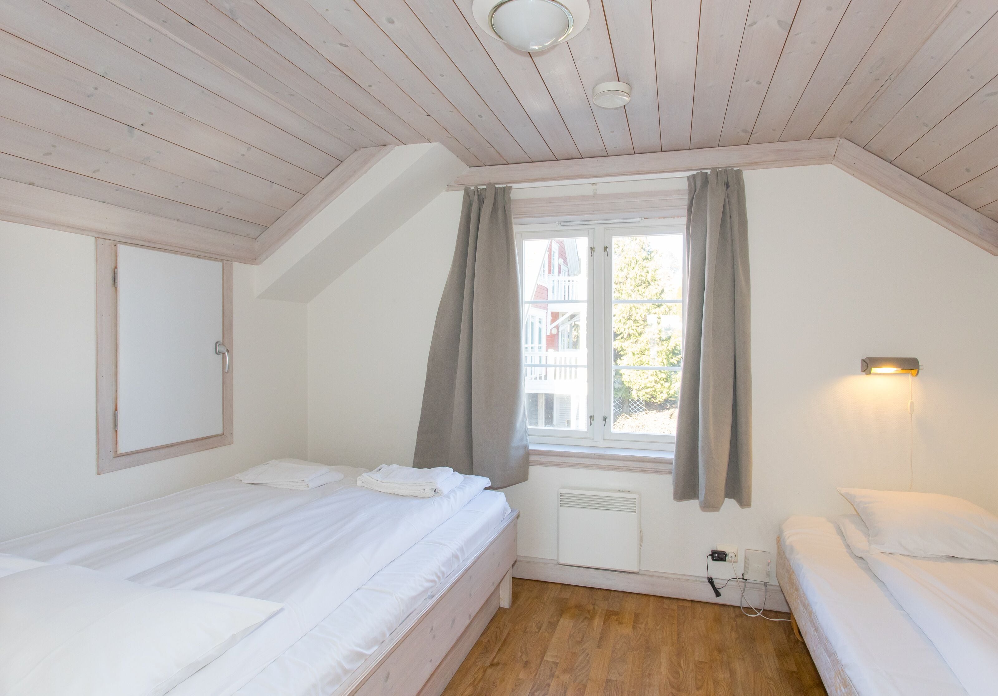 A bedroom with two beds, a window with curtains, a wall-mounted light, and a ceiling fan.
