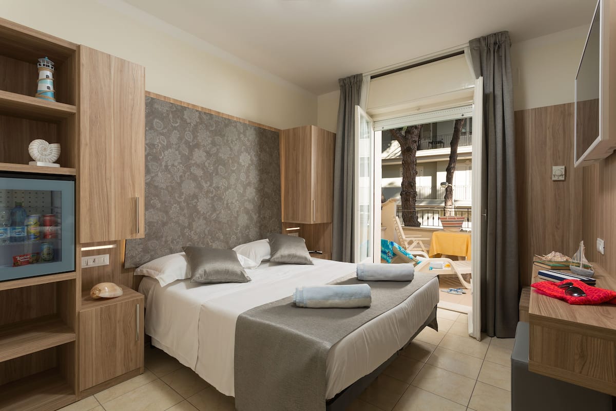 A hotel room with a bed, a desk, a TV, and a view of the outside balcony.