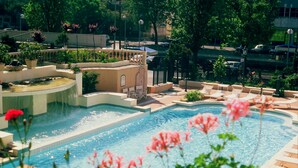 Piscina com cascata, rodeada por espreguiçadeiras e plantas em vasos.