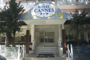 The entrance to Hotel Cannes with a clear sign, steps leading up to the entrance, and a white fence surrounding the area. - Hotel Cannes Riccione (Riccione)