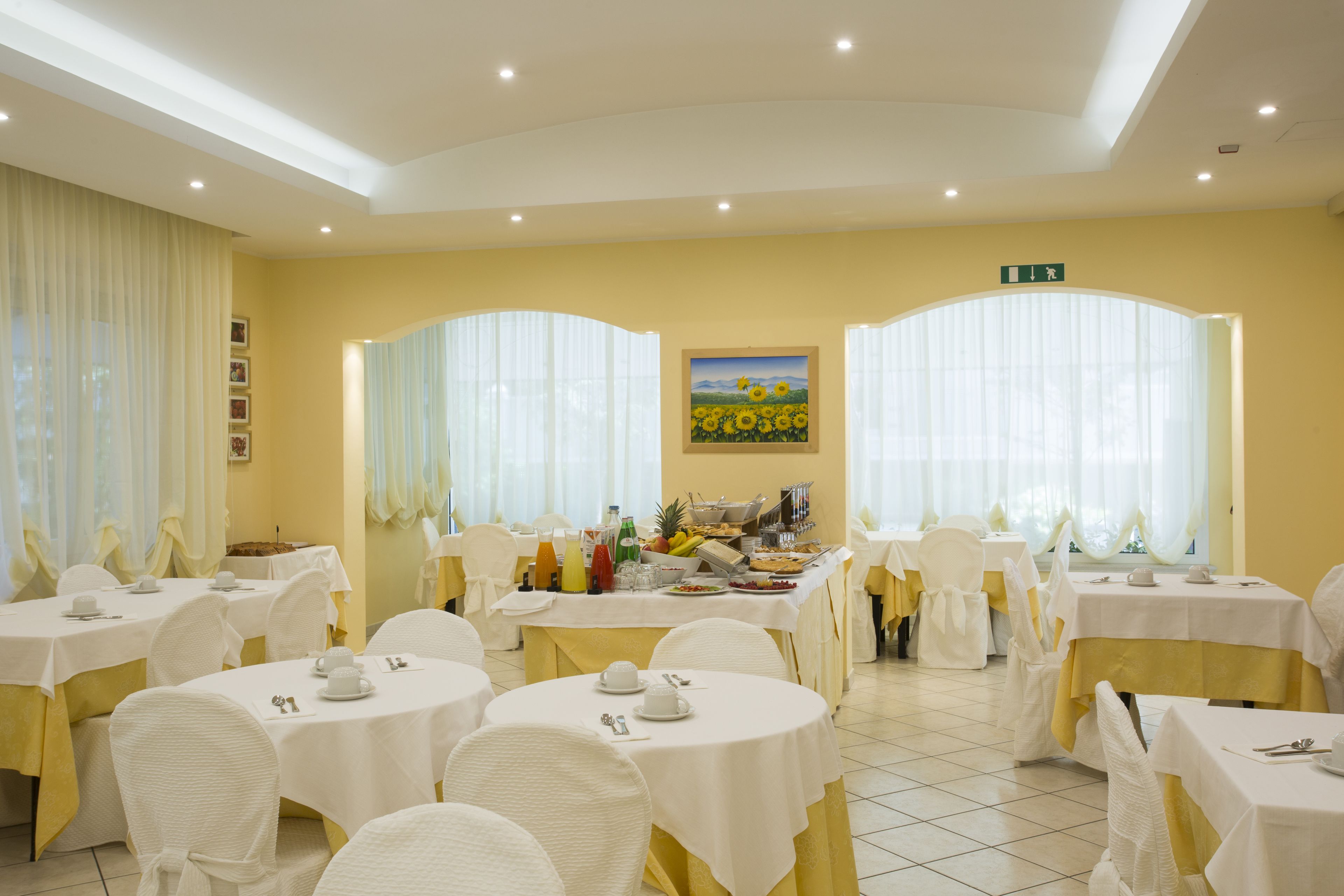 A dining area with round tables, white chairs, and yellow tablecloths.