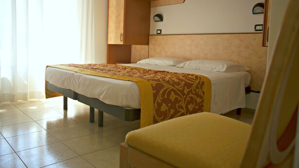 A hotel room with a bed, a chair, and a wardrobe. - Hotel Cannes Riccione (Riccione)