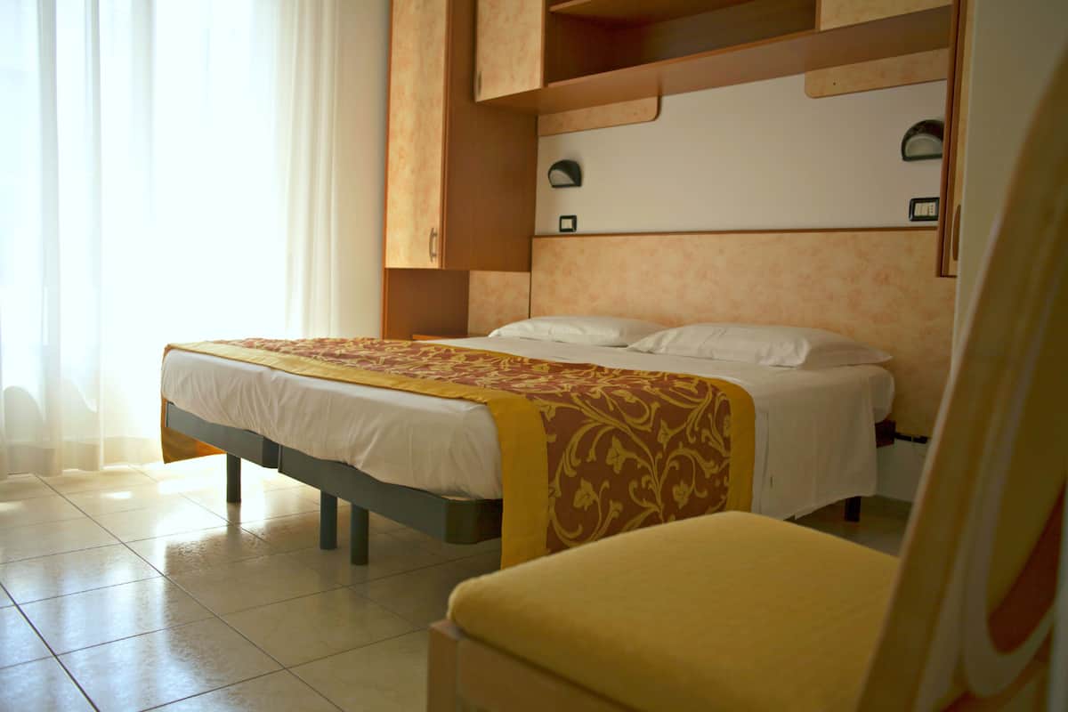 A hotel room with a bed, a chair, and a wardrobe.