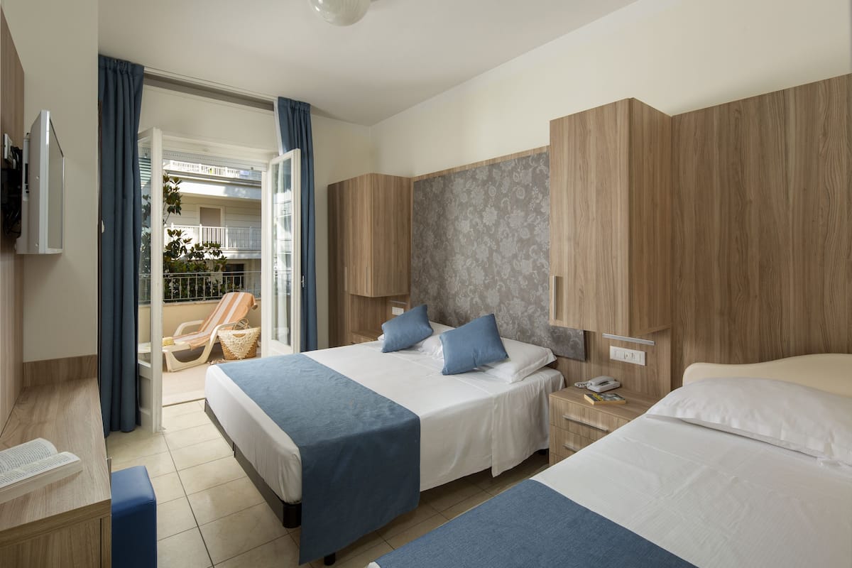 A hotel room with two beds, a balcony with a chair, and a wooden wardrobe.