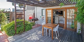 Une terrasse en bois avec une table et des chaises, un barbecue et un coin cuisine équipé d’un téléviseur.