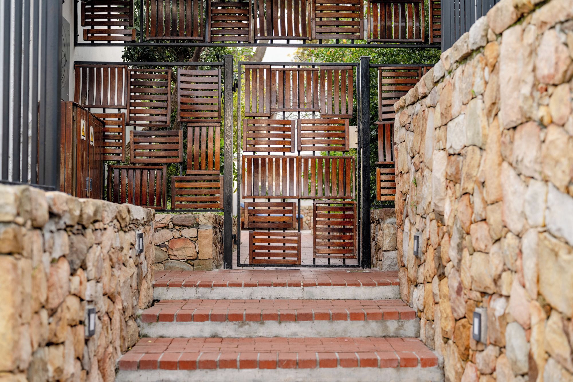Eine Treppe führt zu einem verschlossenen Eingang, an einer Seite eine Steinmauer und auf der anderen ein Metallgitter.