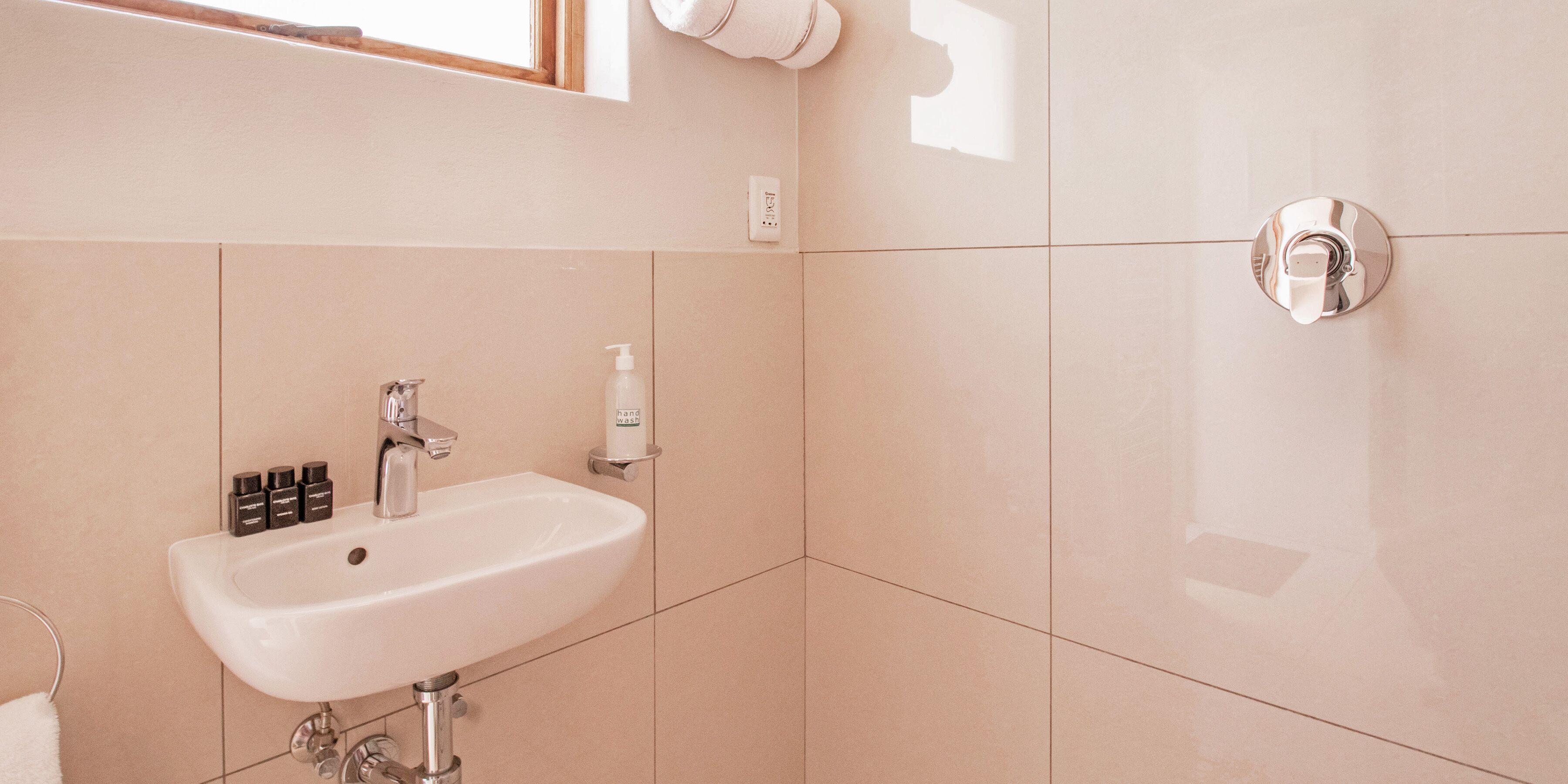Un baño con lavamanos blanco, dispensador de jabón para manos y artículos de tocador.