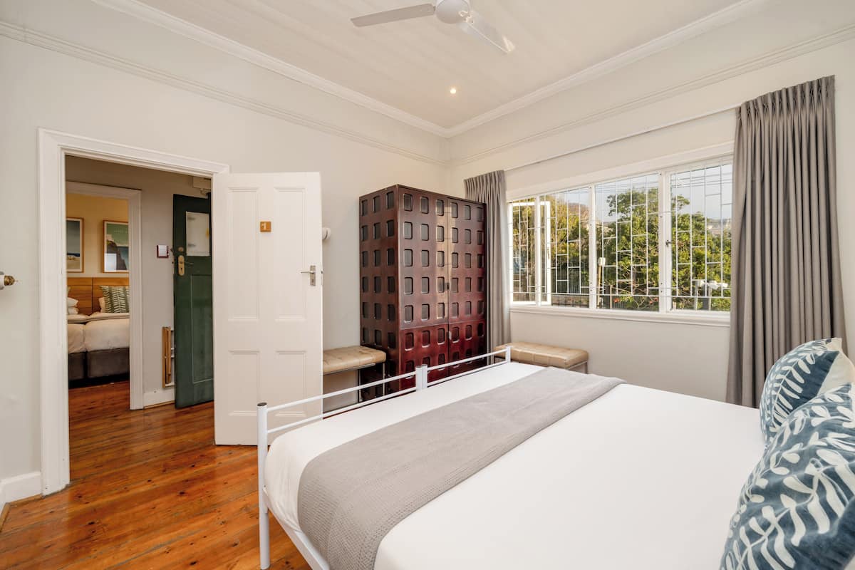 A bedroom with a bed, a window with curtains, a ceiling fan, and a door leading to another room.