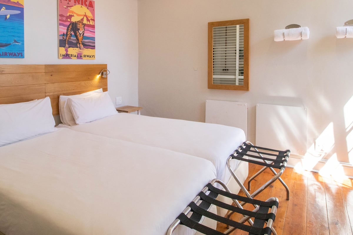 A hotel room with two beds, a wooden headboard, a window with blinds, and a poster on the wall.
