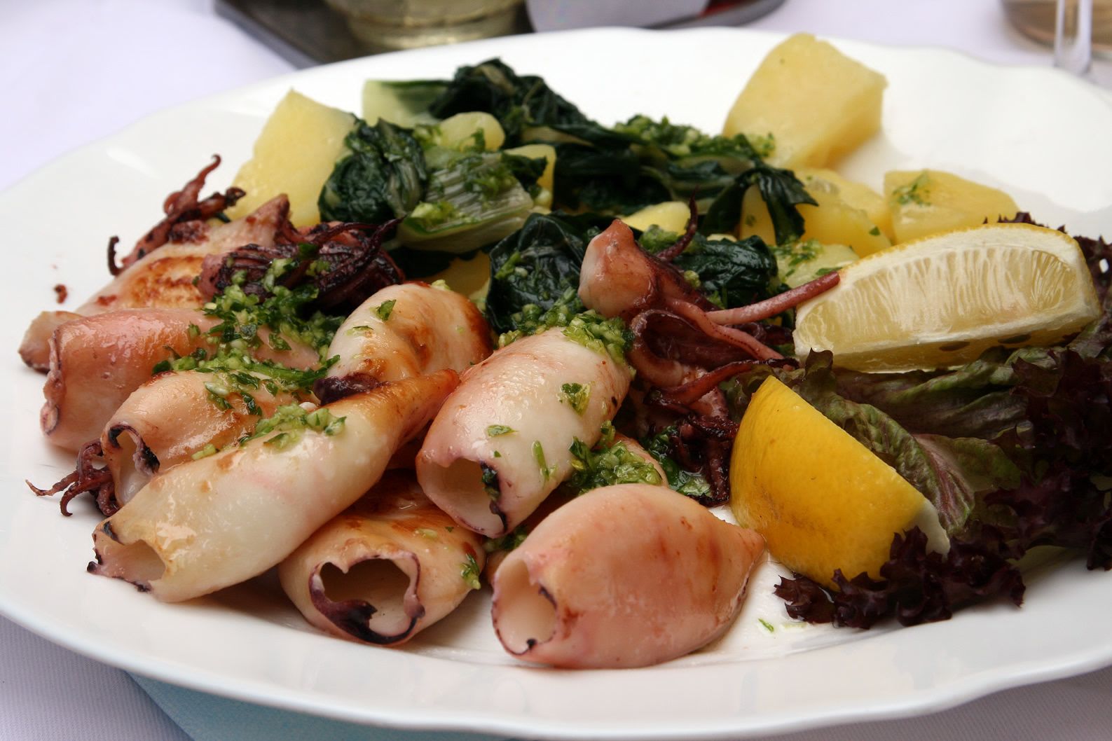 A plate of food with octopus, potatoes, and greens.