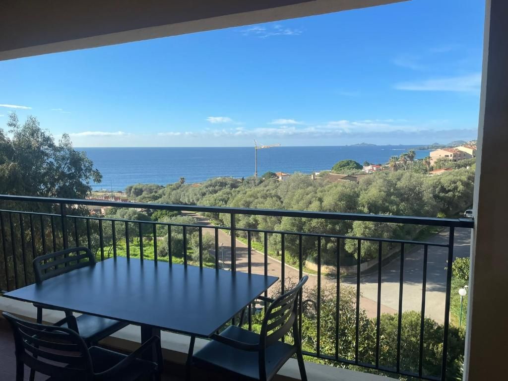 A balcony with a table and chairs, overlooking a coastal landscape with trees and buildings.