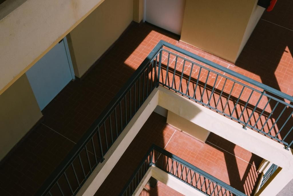Un interior de varios niveles con barandilla metálica, piso de baldosas y paredes en tonos neutros.