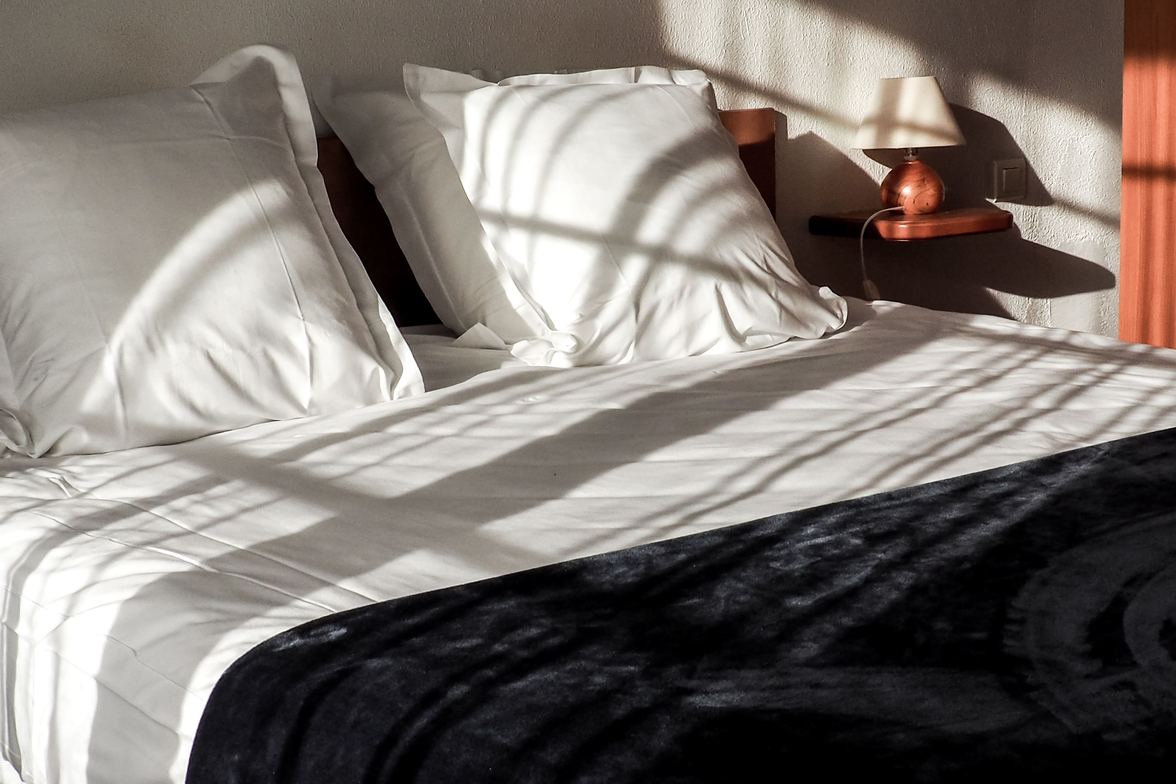 Una cama bien hecha con sábanas blancas y un edredón oscuro.