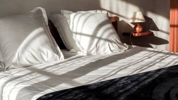 Una cama bien hecha con sábanas blancas y un edredón oscuro.