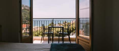 A room with a bed, a table with chairs, and a balcony with a view of the sea.