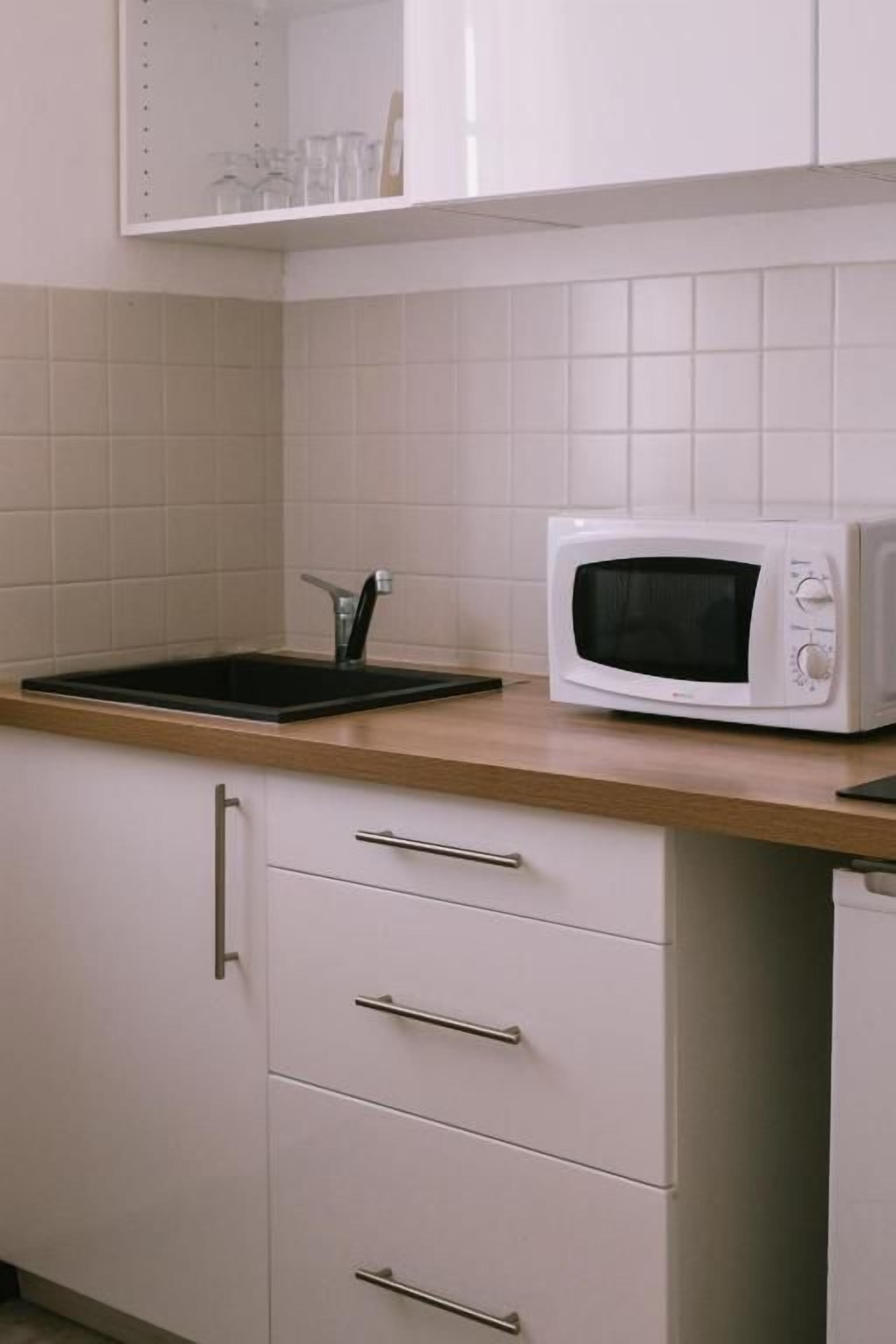 Una cocina con microondas, un lavamanos y un armario con cajones.