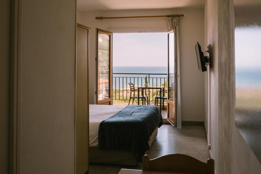 A bedroom with a bed, a chair, and a balcony with a view of the sea.