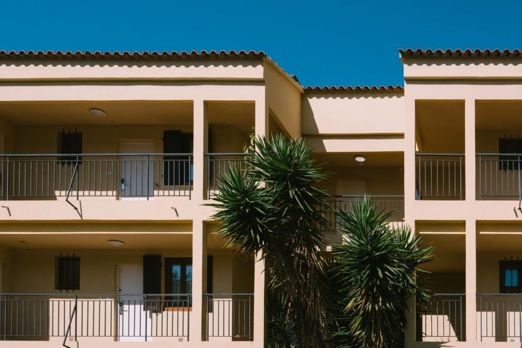 A multi-story building with balconies and a palm tree in the foreground.