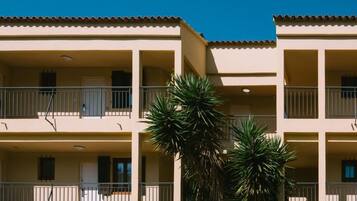 A multi-story building with balconies and a palm tree in the foreground.