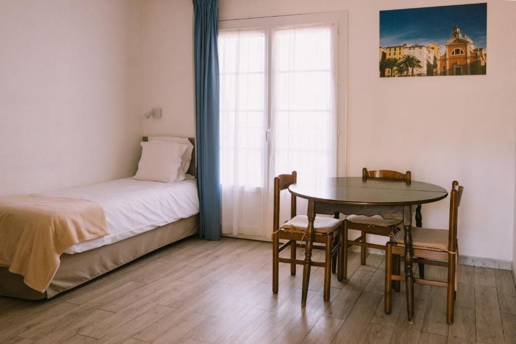 Une chambre à coucher avec un lit, une fenêtre avec des rideaux, une table à manger avec des chaises et un tableau accroché au mur.