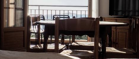Ein Zimmer mit Bett, Tisch, Stühlen, Fernseher und einem Balkon mit Blick.