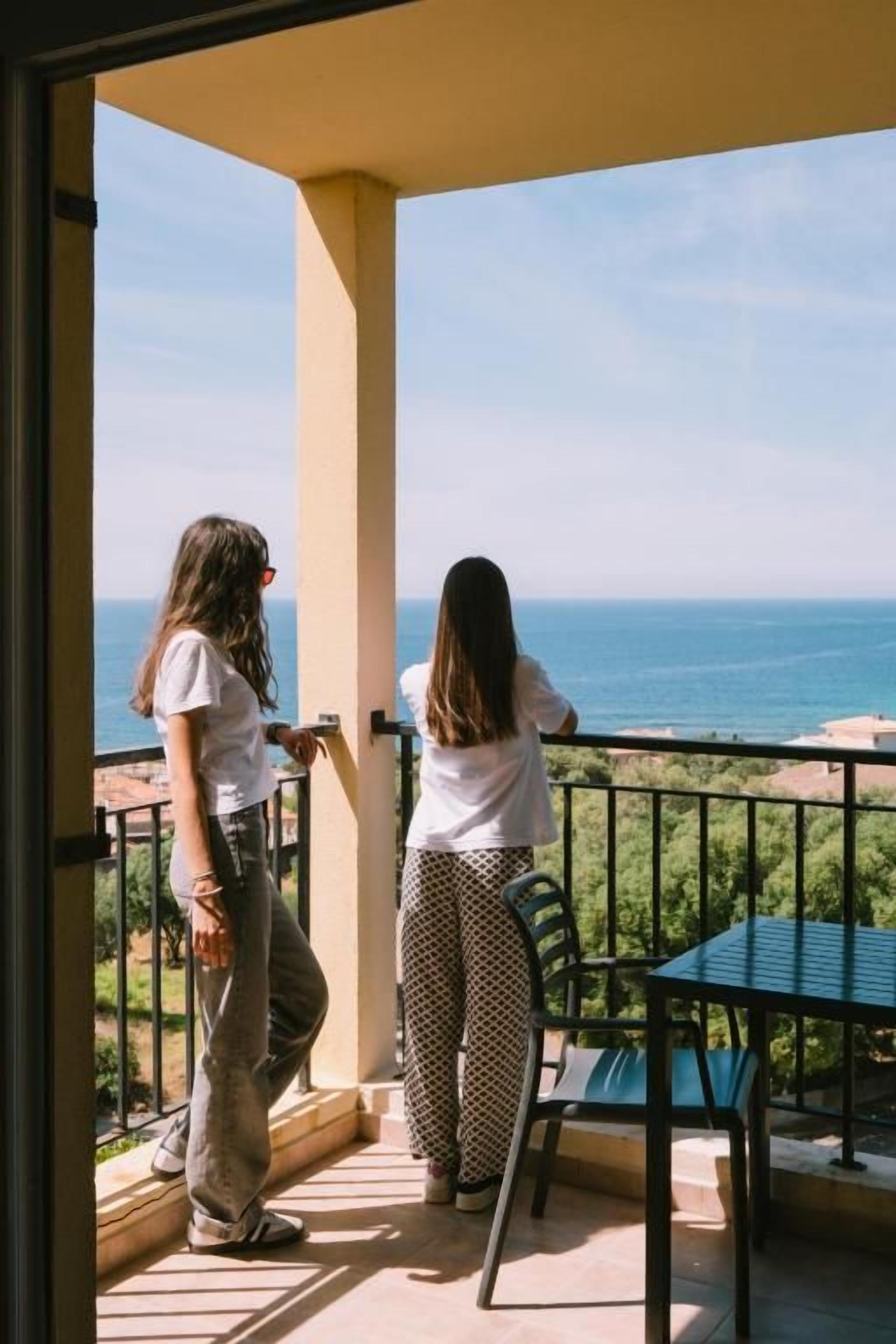 A balcony with a view of the sea, two chairs, and a table.