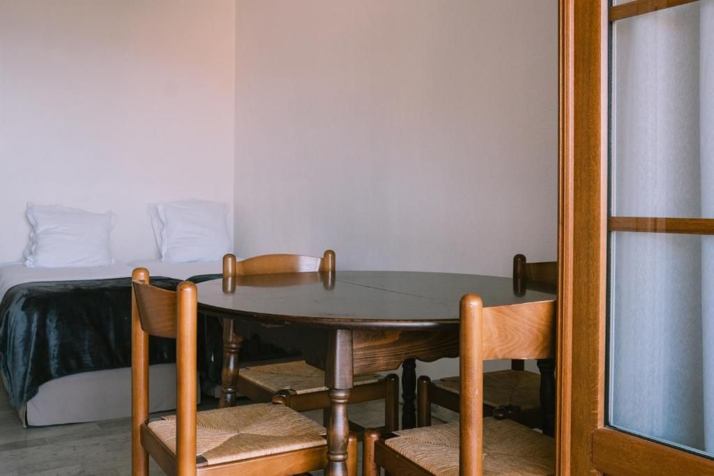 A room with a bed, a round wooden table, and four chairs.