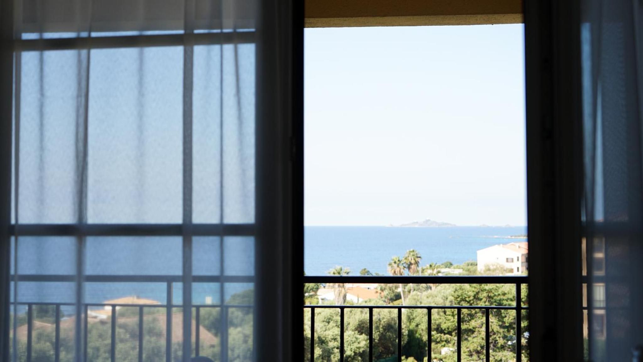 A window with a view of a coastal landscape, including a body of water and distant landforms.