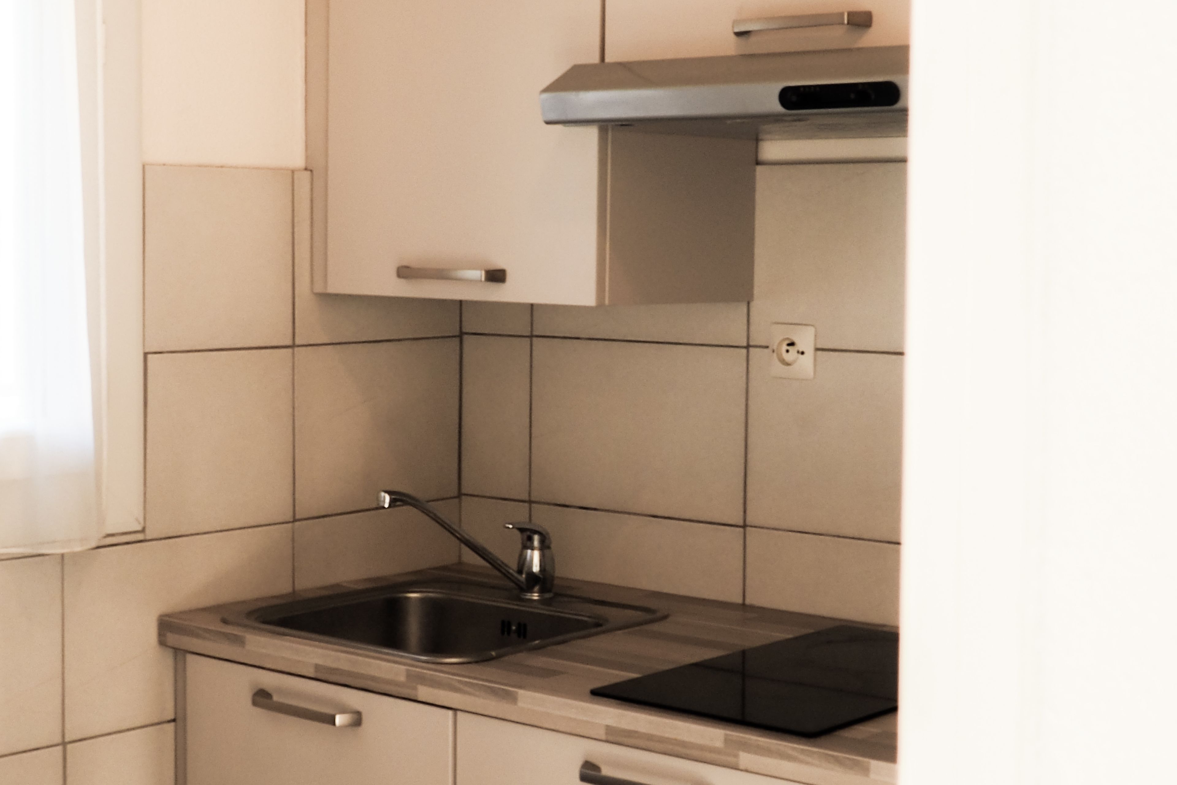 A kitchen with a stainless steel sink, a black induction cooktop, and light-colored cabinets.