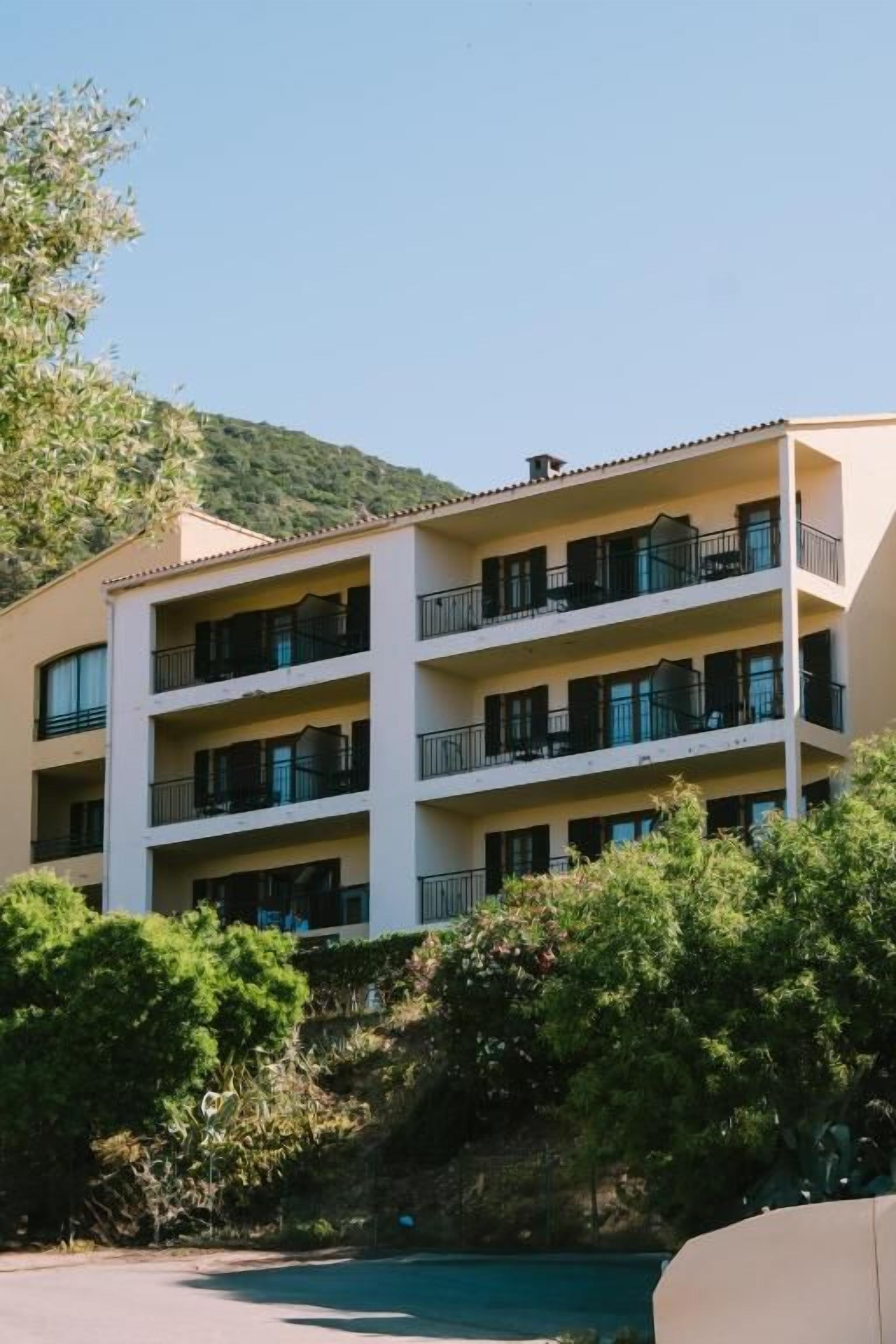 A multi-story hotel with balconies, surrounded by greenery and a pool.