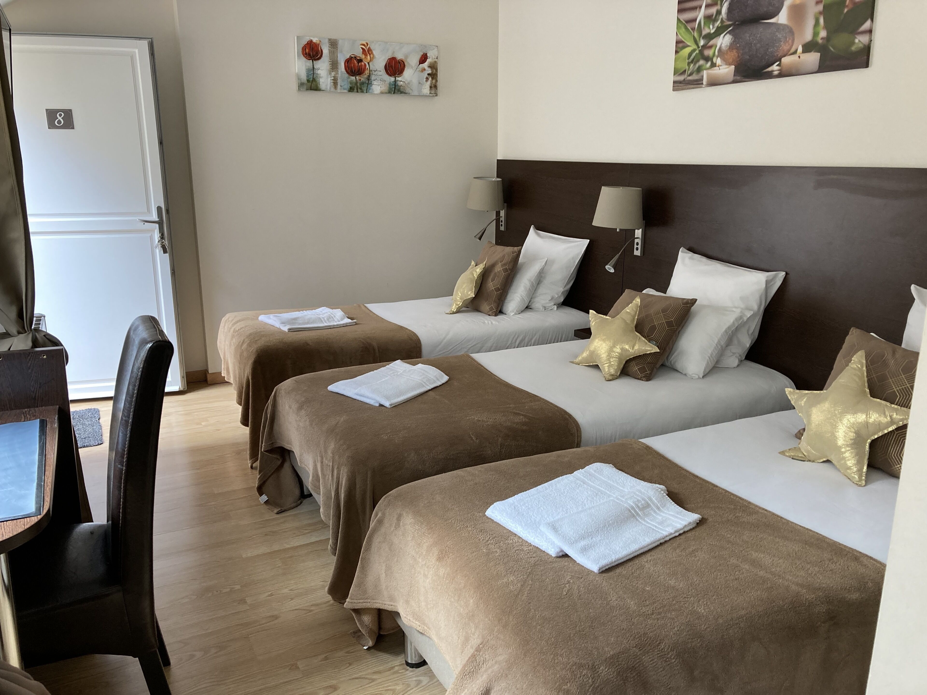 A hotel room with two beds, each with a brown bedspread and white linens, a desk with a chair, and a door marked with the number 8.